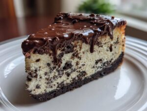 A decadent slice of Oreo cheesecake with chocolate cookie pieces mixed in and topped with a rich chocolate ganache drizzle.