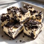 Close-up of several squares of creamy white Oreo fudge loaded with dark chocolate cookie pieces.