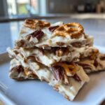 Close-up of stacked white chocolate peanut butter pretzel bark pieces topped with pecans and mini pretzels.