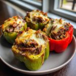 Four baked philly cheesesteak stuffed peppers, topped with melted provolone cheese, served on a grey plate.