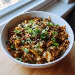 A close-up of a white bowl filled with savory egg roll in a bowl mixture, topped with green onions and sesame seeds.