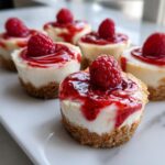 Close-up of several delicious no-bake cheesecake bites topped with raspberry sauce and a fresh raspberry.