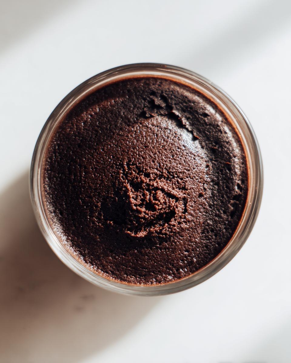 Overhead close-up view of rich, dark chocolate pudding set in a small glass jar.