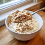 A spoonful of shredded chicken lifted from a bowl of creamy instant pot white chicken chili.