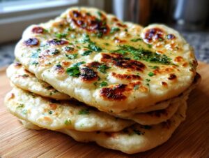 A close-up stack of freshly made naan bread recipe, brushed with butter and topped with chopped parsley.
