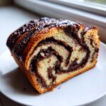 A close-up of a thick slice of chocolate babka showing rich, dark chocolate swirls inside the golden brioche dough.