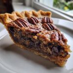 Close-up of a rich slice of chocolate bourbon pecan pie showing the gooey filling, chocolate chips, and pecan topping.