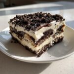 A delicious square slice of layered dirt cake featuring chocolate cookie crumbs and creamy filling, served on a white plate.