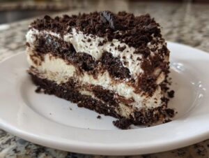 A generous slice of layered dirt cake featuring alternating layers of chocolate cookie crumbs and white creamy filling on a white plate.