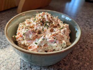 A close-up view of creamy smoked salmon dip mixed with herbs and topped with spices in a small, light green bowl.