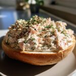 Close-up of a thick layer of creamy smoked salmon dip generously spread on a toasted bagel half, topped with dill and spices.
