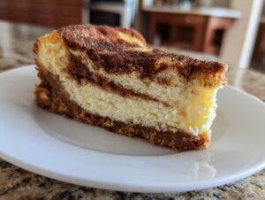 A close-up of a perfect slice of snickerdoodle cheesecake showing the creamy filling and cinnamon swirl topping on a white plate.