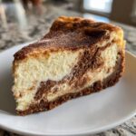 Close-up of a perfect slice of snickerdoodle cheesecake showing the creamy white filling swirled with cinnamon spice on a white plate.