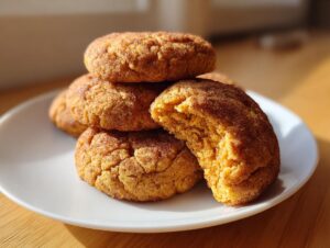 A stack of soft, thick pumpkin snickerdoodle cookies coated in cinnamon sugar, with one cookie broken open showing the moist interior.