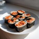 Close-up of several slices of spicy tuna kimbap arranged on a white plate, showing the rice, nori wrap, and bright orange tuna filling.