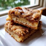 Two delicious snickerdoodle blondies stacked on a white plate, showing a thick, chewy base and a cinnamon swirl topping.