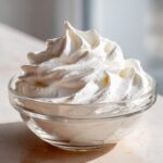 A glass bowl filled with stiff, perfectly piped white icing, resembling peaks, illustrating a successful royal icing recipe.