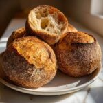A stack of four rustic, crusty sourdough bread bowls, one cut open showing an open crumb structure.