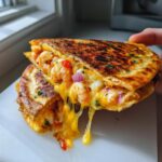 A hand holds a perfectly grilled shrimp quesadilla cut in half, showing abundant melted cheese and plump shrimp filling.