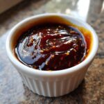 Close-up of thick, glossy homemade teriyaki sauce with visible sesame seeds in a small white ramekin.