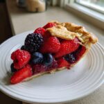 A generous slice of triple berry pie loaded with strawberries, raspberries, blueberries, and blackberries on a white plate.