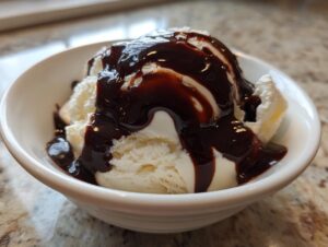 A scoop of vanilla ice cream generously covered in homemade chocolate syrup in a white bowl.