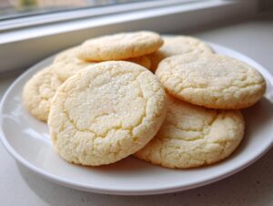 A stack of freshly baked, round vegan sugar cookies sprinkled with coarse sugar, resting on a white plate.