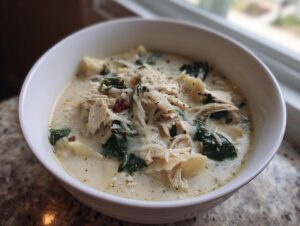 A close-up of a white bowl filled with creamy white chicken lasagna soup, featuring shredded chicken, spinach, and pasta.