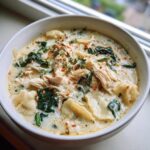A close-up of a hearty bowl of white chicken lasagna soup, featuring shredded chicken, pasta, spinach, and red pepper flakes.