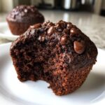 A close-up of a rich, dark chocolate muffin with melted chocolate chips, showing a bite taken out. Perfect for a chocolate muffins recipe.