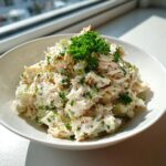 A bowl of creamy crab salad mixed with celery and topped with fresh parsley, ready to eat.