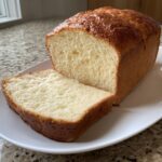 A golden-brown loaf of keto cottage cheese bread, partially sliced on a white plate.
