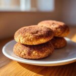 A stack of soft, thick snickerdoodle cookies generously coated in cinnamon sugar, resting on a white plate.