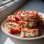 Stack of delicious italian pinwheels made with salami and cream cheese filling, garnished with herbs.