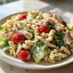 Close-up of a healthy chicken caesar pasta salad with rotini pasta, shredded chicken, and cherry tomatoes.