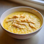 Close-up of a bowl filled with creamy, yellow chicken lemon rice soup topped with shredded chicken.