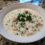 A close-up of creamy chicken and rice soup garnished with fresh parsley in a white bowl.