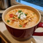 A close-up of creamy chicken tortilla soup instant pot in a red mug, topped with sour cream and tortilla strips.