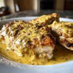 Three pieces of seared chicken breasts generously covered in a rich, yellow, creamy dijon chicken sauce.