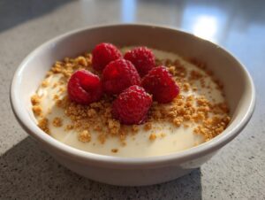 Close-up of a creamy protein cheesecake bowl topped with fresh raspberries and graham cracker crumbs.