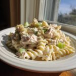 A close-up of creamy tuna noodle salad cold made with rotini pasta and celery chunks, served on a white plate.