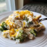 A spoonful of creamy crockpot chicken and rice broccoli topped with melted cheddar cheese being lifted from a white plate.