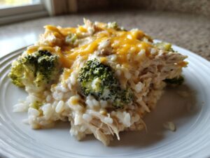 A close-up serving of creamy crockpot chicken and rice broccoli topped with melted cheddar cheese on a white plate.