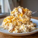 A spoonful of creamy easy crockpot chicken and rice topped with melted cheddar cheese being lifted from a white plate.