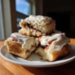 Three fluffy cinnamon rolls homemade stacked on a white plate, generously topped with cream cheese frosting.