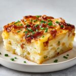 A thick, square slice of french onion potato bake showing layers of potatoes, creamy filling, and caramelized onions.