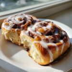 Two soft, glazed apple cinnamon rolls sitting on a white plate, with one slightly torn open.