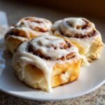 Close-up of three freshly baked cinnamon rolls generously topped with thick white icing.