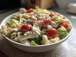 Close-up of a bowl filled with healthy chicken caesar pasta salad, featuring rotini pasta, shredded chicken, and cherry tomatoes.