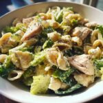 Close-up of a bowl filled with high protein chicken caesar pasta salad featuring shell pasta, romaine lettuce, and chunks of chicken.